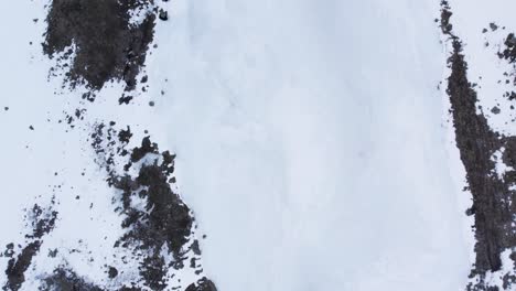 Drohnenaufnahmen-Aus-Der-Luft-über-Gefrorenem-Eis,-Schnee,-Felsen-Und-Felsbrocken-In-Den-Cairngorms-In-Schottland-Im-Winter,-Die-Vorwärts-Und-über-Eine-Steile-Klippe-Fliegen,-Um-Ein-Eisiges-Flusstal-Und-Schneebedeckte-Berge-Zu-Enthüllen