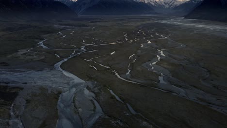 Aerial-shot-of-beautiful-mountains-above-a-valley-with-rivers-running-through-during-sunrise,-rising-shot