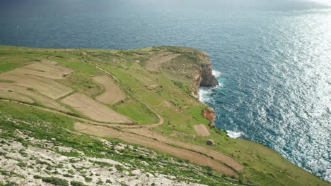 AERIAL:-Greenery-Plains-of-Ta-Cenc-Cliffs-near-Blue-Mediterranean-Sea-on-Windy-Day