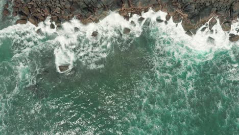 Aerial-drone-view-of-waves-crashing-against-the-rocks-on-a-beach