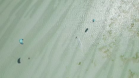 Top-view-tracking-shot-of-kiteboarder-surfing-over-tropical-beach-shoals-on-bright,-sunny-day