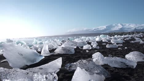 Ice-chunks-melting-on-black-Diamond-beach-in-Iceland,-mountains-beyond