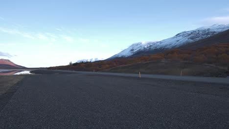 Car-driving-on-an-asphalt-road-in-a-mountain-valley-at-dusk,-Iceland