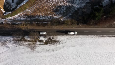 A-driving-concrete-mixer-vehicle-passes-the-snowy-landscape,-top-down-with-slow-zoom-out