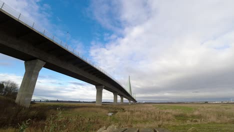 Speeding-time-lapse-clouds-passing-over-suspension-bridge-on-rural-countryside-marshland-development