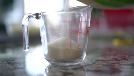 Pouring-cane-sugar-into-glass-measuring-cup-for-recipe-for-certain-quantity