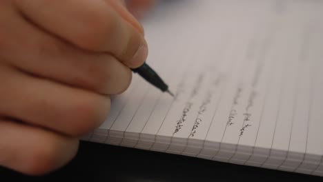 Extreme-close-up-of-a-man-writing-on-a-notebook-with-a-black-pen