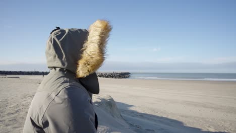 Person-with-hooded-jacket-feeling-the-North-Sea-breeze-on-a-beautiful-windy-day-in-Ostend,-Belgium---Concept-of-mental-rest,-reflection,-body-and-soul