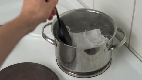 Man-sanitizing-a-used-face-mask-by-putting-it-into-boiling-water