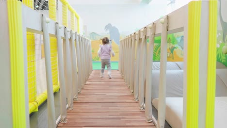 Slow-motion-of-a-happy-child-running-on-a-shaky-bridge-at-Indoor-playground-for-children--back-view