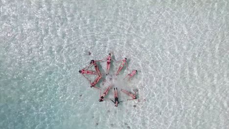 women-holding-hands-floating-on-blue-water-sea-forming-a-star,-Synchronized-swimming,-drone-top-view