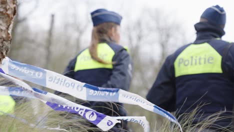 Polizeiband-Weht-Im-Wind-Gegen-Polizisten,-Die-Am-Abgesperrten-Tatort-Auf-Unterstützung-Warten