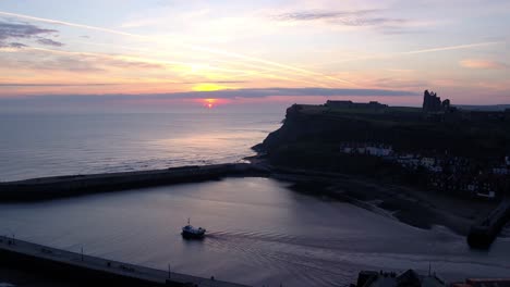 Whitby-harbour-mouth,-static-drone-shot-at-blue-hour-sunrise-with-boat-sailing-to-open-sea---DJI-Inspire-2