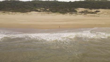 Luftaufnahme-Eines-Mannes,-Der-An-Sonnigen-Tagen-Am-Strand-Von-Playa-Grande-In-Punta-Del-Diablo,-Uruguay,-Läuft---Wellen,-Die-Sand-Und-Dünen-Im-Hintergrund-Erreichen