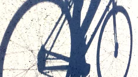 Sombra-De-Un-Hombre-En-Bicicleta-Por-Una-Pista-De-Tierra-Bajo-El-Sol-Brillante