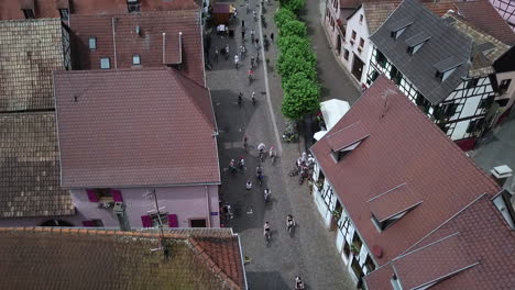 A-stationary-top-view-aerial-footage-of-passing-cyclists-passing-through-the-streets-of-the-village