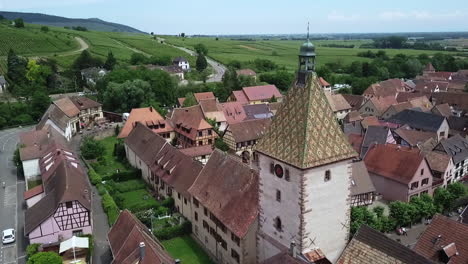 A-smooth-drone-shot-revolving-around-the-clock-tower-while-revealing-the-grassland,-some-crops-and-the-whole-village