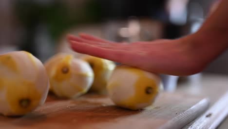 A-stationary-shot-of-a-woman's-hands-while-rolling-a-peeled-lemon-against-the-chopping-board-and-cutting-it-in-half