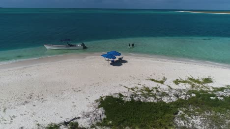 Drohne-Schoss-Atemberaubende-Karibische-Strandinsel-Mit-Boot-Und-Paar,-Das-Im-Blauen-Wassermeer-Schwimmt