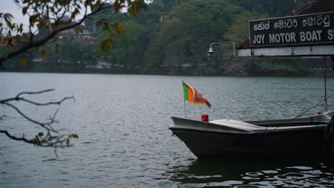 Small-flag-with-a-golden-lion-waving-in-the-wind-on-the-front-of-a-motorboat-moored-at-a-mooring-with-a-sign-in-Sinhala-and-English-language-above-the-jetty-at-Kandy-Lake-in-Sri-Lanka