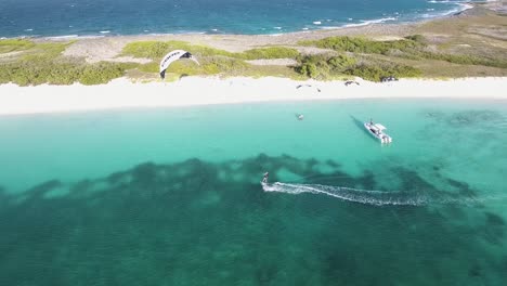MAN-Kitesurf-RIGHT-TO-LEFT-shore-beach,-white-sand-and-turquoise-water,-Los-Roques,-Drone-shot