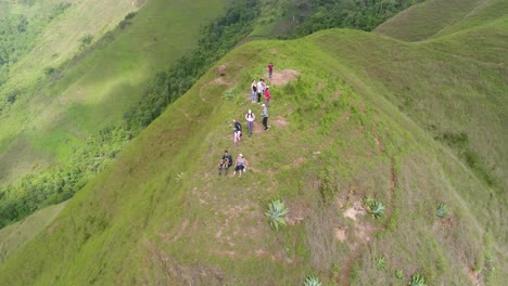 Drone-turn-360-degree-over-group-people-climb-on-top-mountain,-green-tropical-landscape