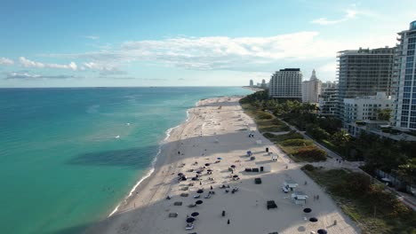 Aerial-drone-view-over-people,-parasols-and-waves-on-the-Miami-beach-in-sunny-Florida,-backwards-revealing,-drone-shot