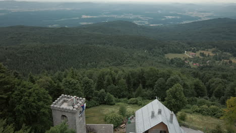 Drone-shot-from-afar-in-the-air-of-valley,-tower-and-mountain-cottage