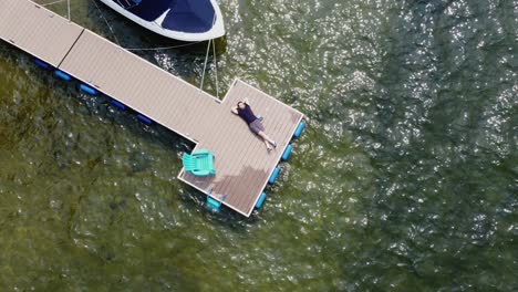 Drone-shot-of-a-man-laying-on-a-dock-enjoying-a-clear,-sunny-day-at-Lake-Payette-in-McCall,-Idaho