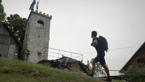 Low-perspective-of-a-young-hiker-walking-past-the-monutain-cottage-towards-the-tower