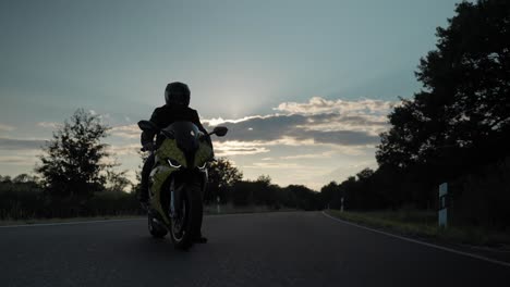 Shot-of-a-man-standing-on-his-motorcycle-in-the-middle-of-the-road-on-a-freeway-in-countryside-during-the-sunset