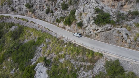 Long-drone-shot-of-a-car-driving-down-a-windy-mountain-road-on-a-sunny-afternoon-in-Sa-Calobra,-Mallorca,-Spain