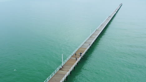 Aerial-4K-Drone-Flyover-Long-Pier-Boardwalk-With-Athlete-Running-Along-Pathway