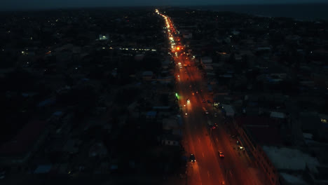 Filmische-4k-Luftdrohnenaufnahme-Des-Nächtlichen-Straßenverkehrs-Mit-Autos,-Die-Während-Der-Hauptverkehrszeit-In-Einer-Afrikanischen-Stadt-In-Der-Nähe-Des-Ozeans-Fahren---Lomé,-Togo