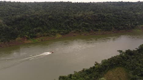 Aerial-tracking-shot-of-speedboat-cruising-on-idyllic-river-border-between-Brazil-and-Argentina-surrounded-by-Amazon-River