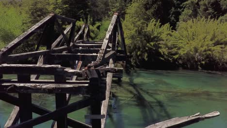 Drone-Flying-around-wooden-bridge-across-the-river,-7-lakes-route,-Argentina