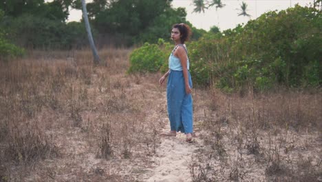Mujer-Con-Traje-Azul-Caminando-Por-Un-Sendero-De-Playa-Con-Hierba-Seca-Y-Mirando-Hacia-Atrás