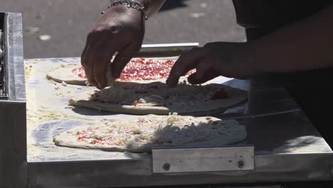 Close-up,-chef-spreading-toppings-on-pizza-outdoors-to-prepare-for-baking