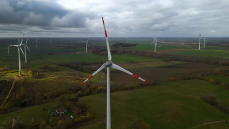 Aerial-shot-of-multiple-rotating-windmills-for-renewable-electric-power-production-in-a-wide-rural-area-on-a-cloudy-day