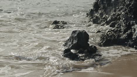 Waves-on-sandy-beach-from-ocean-crashing-against-black-volcanic-rocks
