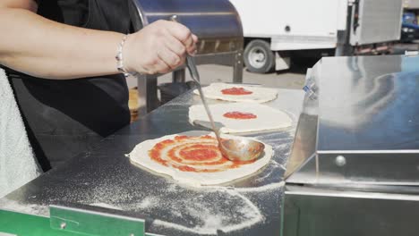 Close-up,-woman-spreading-tomato-sauce-on-pizza-dough-with-ladel-outdoors-in-slow-motion