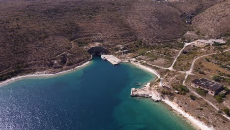 Luftaufnahme-Eines-Türkisfarbenen-Strandes-Mit-Verlassenen-Kommunistischen-Strukturen-An-Der-Albanischen-Riviera