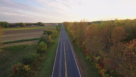 FPV-drone-slowly-flying-down-rural-asphalt-road-during-golden-hour-in-fall-season