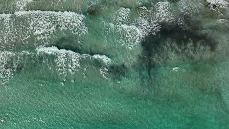 Top-down-view-of-waves-hitting-beach-in-slowmotion-going-forward