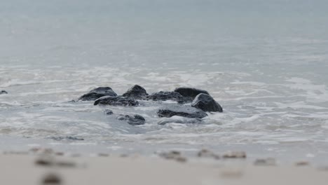 Black-stones-on-beach-being-engulfed-by-waves-splashing-on-them