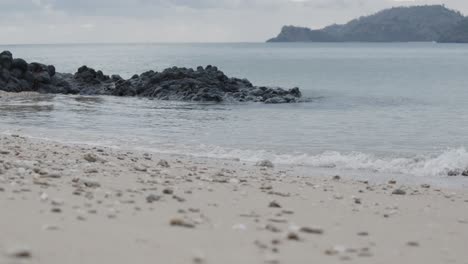 Ocean-waves-crashing-on-beach-and-black-rocks-on-an-island