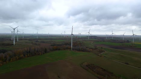 Aerial-shot-of-multiple-spinning-wind-turbines-for-renewable-electric-power-production-in-a-wide-rural-area-on-a-cloudy-day