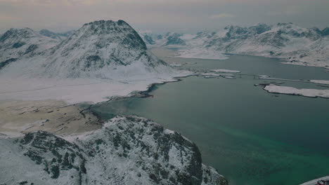 Lofoten-snow-covered-Ramberg-extreme-mountain-terrain-and-blue-glacial-Nordic-ocean-aerial-view-over-landscape