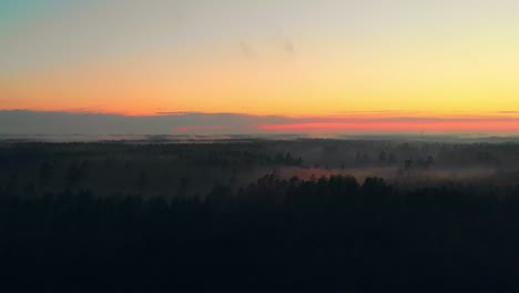 Misty-landscape-with-forest-in-sunset-colours,-panoramic-view-over-the-trees,-pan-right