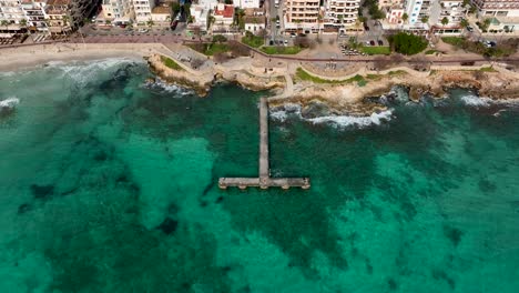 Town-down-reveal-of-empty-dock-and-city-of-Cala-Millor-on-Mallorca,-Spain